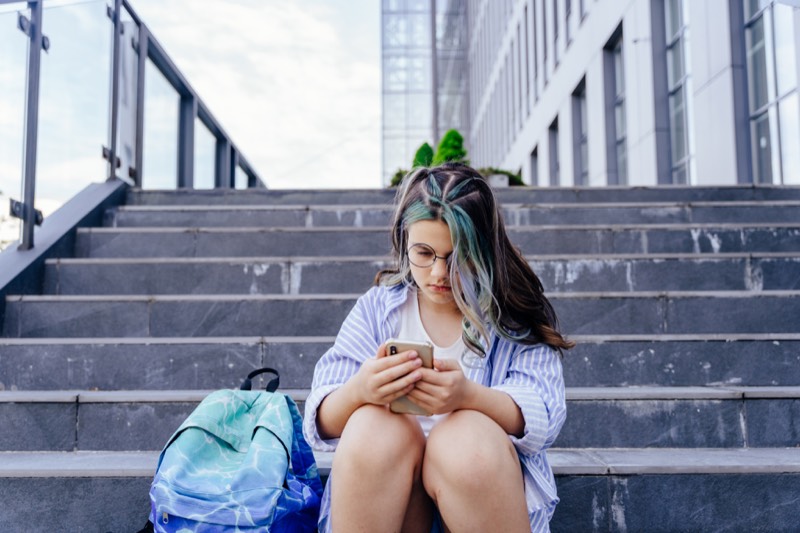 Young person sitting on outdoor stairs and looking at a phone